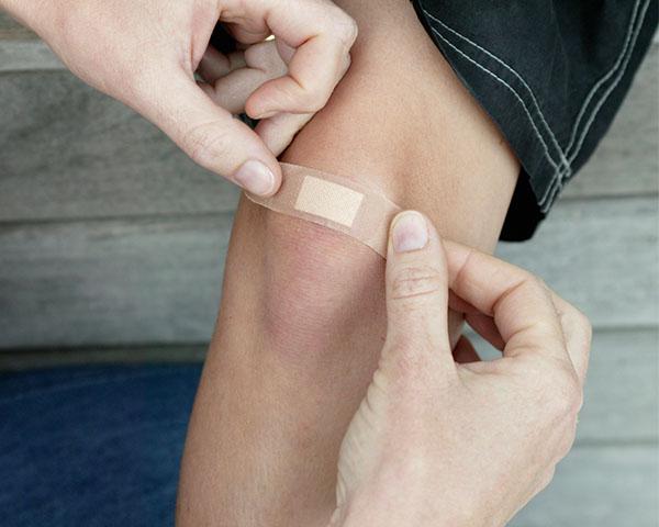 Personne qui couvre une plaie mineure à un genou avec un pansement Band-Aid®
